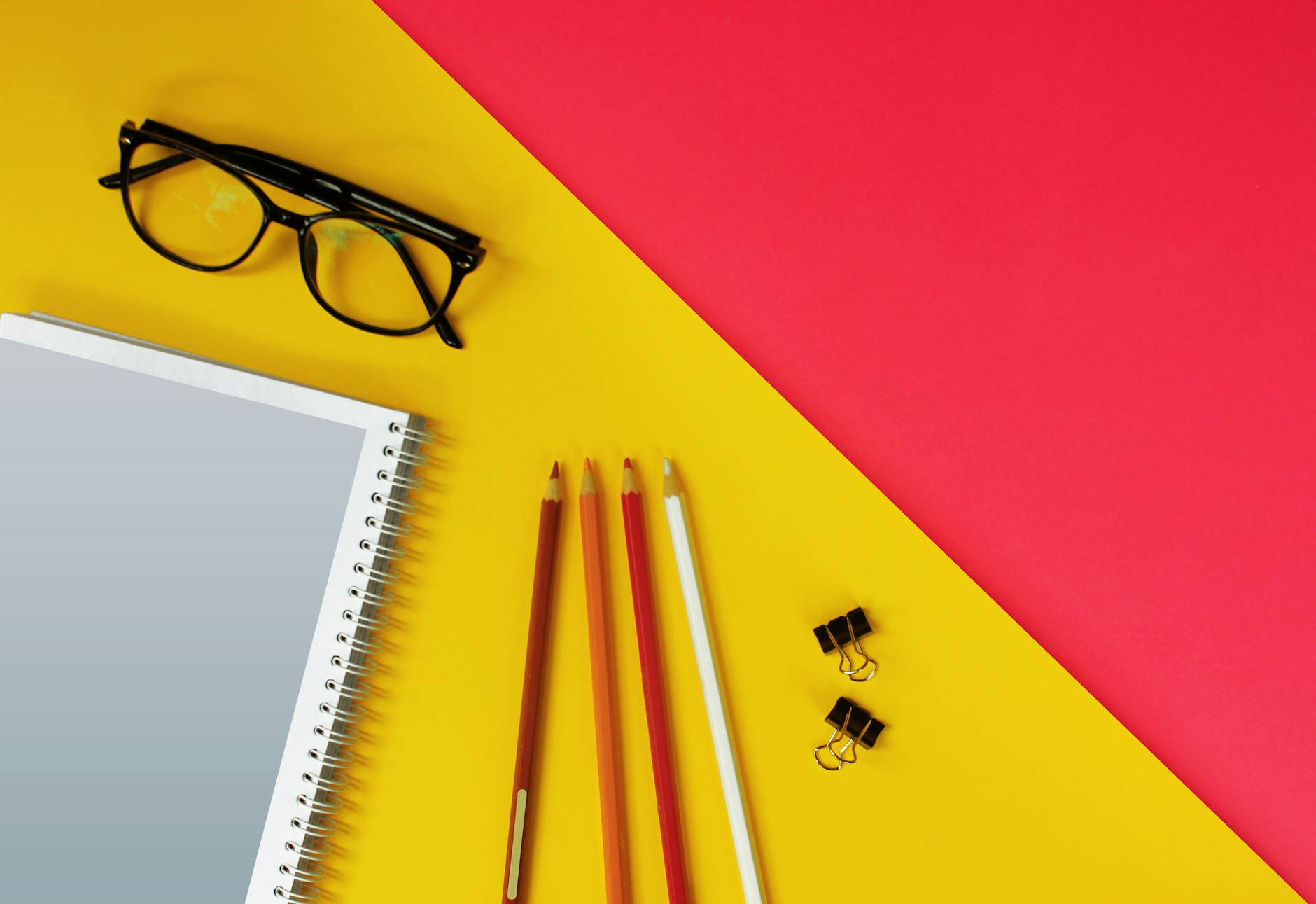 black framed eyeglasses beside white pencil on pink table